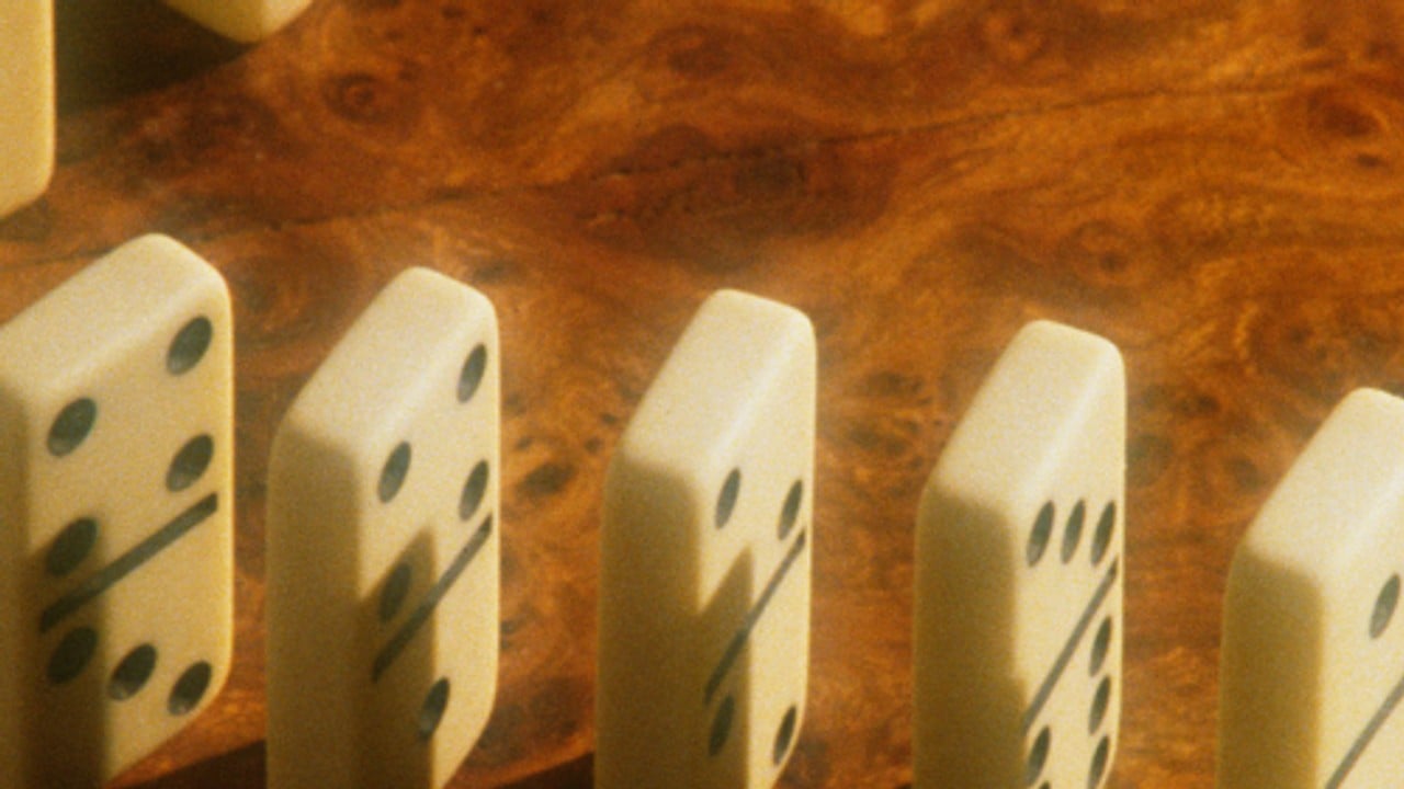 A row of dominoes mid-fall on a dark wooden surface