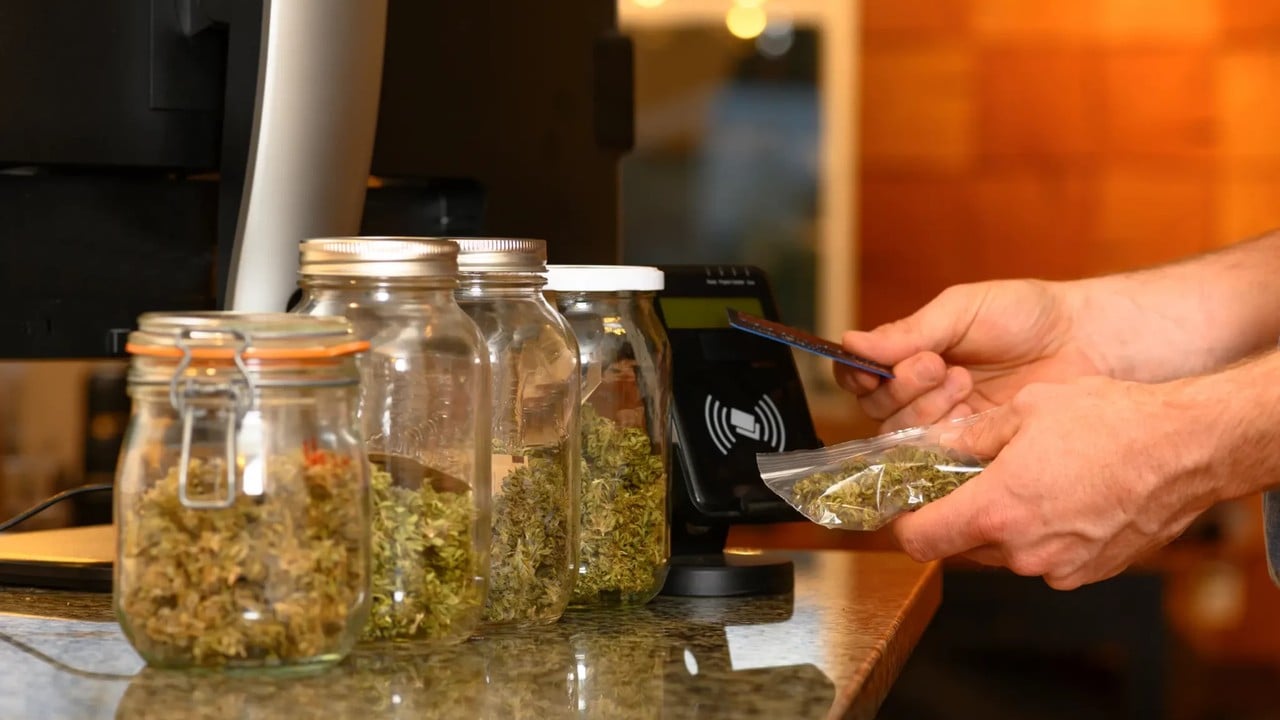 A hand tapping a card reader on a shop counter beside glass jars