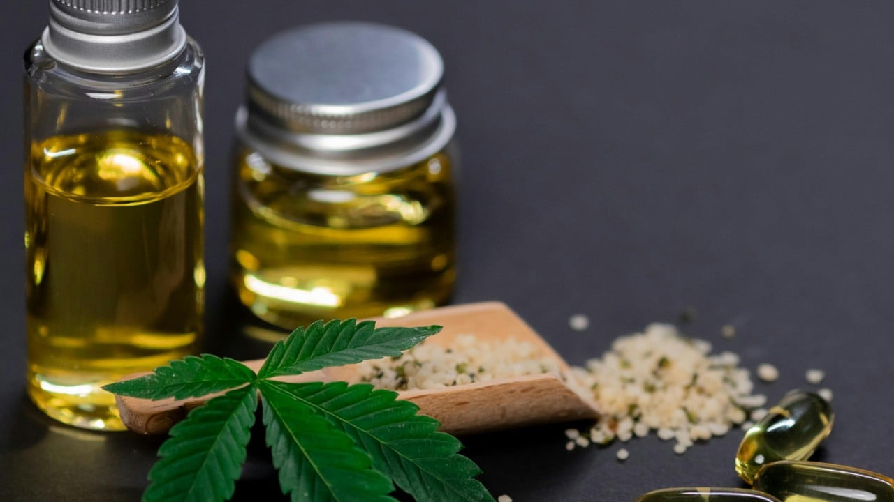 Jars of hemp oil and softgel capsules beside a cannabis leaf